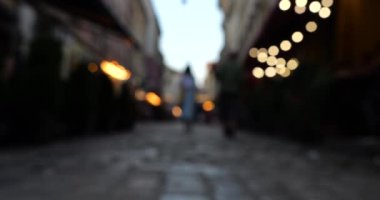 Garland lights and people in the evening cafe and on the street. European city architecture. Out of focus.