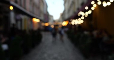 Garland lights and people in the evening cafe and on the street. European city architecture. Out of focus.