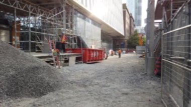 Construction workers in uniforms and helmets throw construction waste into a container. Downtown Toronto, Ontario, Canada. Out of focus.