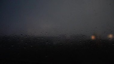 Penceredeki yağmur damlalarının arasından gökyüzünde şimşek çakıyor.