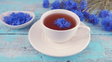 Composition with knapweeds flowers in white and blue colors on vintage light blue wooden tabletop. Brewing a tisanes from knapweeds flowers in white cup.