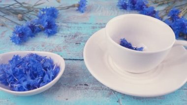 Composition with knapweeds flowers in white and blue colors on vintage light blue wooden tabletop. Brewing a tisanes from knapweeds flowers in white cup.