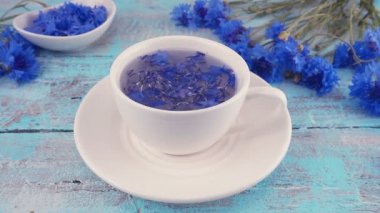 Composition with knapweeds flowers in white and blue colors on vintage light blue wooden tabletop. Brewing a tisanes from knapweeds flowers in white cup.