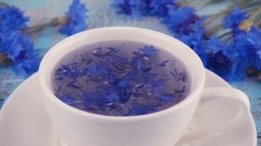 Knapweed çiçekli kompozisyon beyaz ve mavi renkte açık mavi ahşap masa üstünde. Knapweed 'lerden demlenen çiçekler beyaz bardakta.