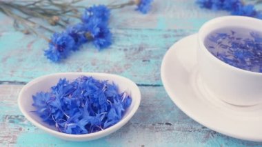 Composition with knapweeds flowers in white and blue colors on vintage light blue wooden tabletop. Brewing a tisanes from knapweeds flowers in white cup.
