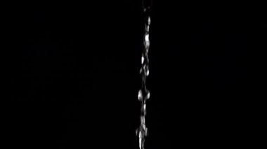 Bir su akıntısı düşer ve siyah arka planda bir sıçrama yaratır. Yavaş çekim.