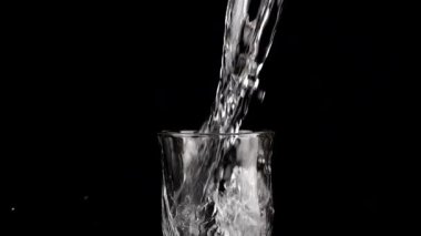 Siyah bir zemin üzerinde cam kadehlere bir su püskürtülür ve bir su sıçramasına neden olur. Yavaş çekim.