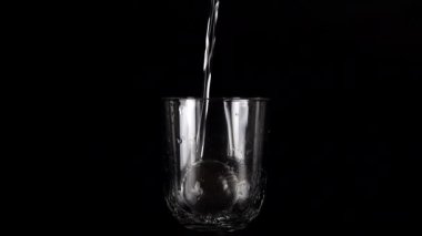 Siyah bir zemin üzerinde cam kadehlere bir su püskürtülür ve bir su sıçramasına neden olur. Yavaş çekim.