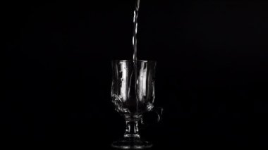 Siyah bir zemin üzerinde cam kadehlere bir su püskürtülür ve bir su sıçramasına neden olur. Yavaş çekim.