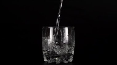 Siyah bir zemin üzerinde cam kadehlere bir su püskürtülür ve bir su sıçramasına neden olur. Yavaş çekim.