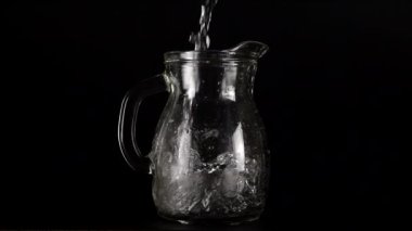 Bir su püskürtüsü, siyah bir zemindeki cam bir sürahiye dökülür ve bir su sıçramasına neden olur. Yavaş çekim.
