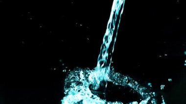 Bir su akıntısı düşer ve siyah arka planda bir sıçrama yaratır. Yavaş çekim.