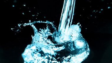 Bir su akıntısı düşer ve siyah arka planda bir sıçrama yaratır. Yavaş çekim.