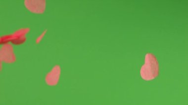 Yeşil arka planda kalp şeklinde konfeti düşüyor..