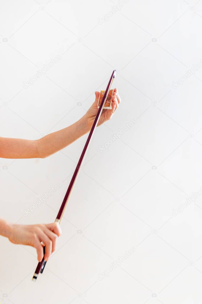 hands of a young violinist rosin his bow on a light background, vertical