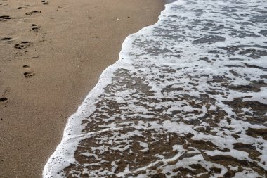 Bulanık deniz arka planında köpüklü kumlu plaj manzaralı, yatay.