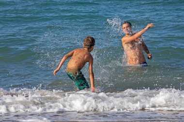 Mutlu baba ve oğlu güneşli bir günde denizde oynuyorlar, yatay olarak.