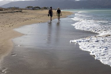 Birbirlerine aşık çiftler, güneşli bir günde deniz kıyısında yürüyorlar.