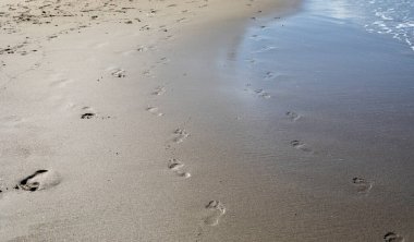 Deniz kıyısındaki kumsaldaki ıslak kumda yatay ayak izlerinin soyut arkaplanı.