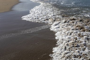 Bulanık deniz arka planında köpüklü kumlu plaj manzaralı, yatay.