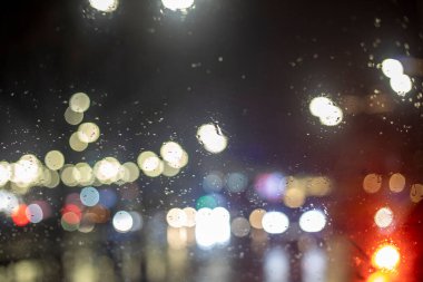 Yağmurda trafik sıkışıklığı sırasında parlak ışıkları olan ve geç kalan bir arabanın ön camındaki bulanık arka plan.