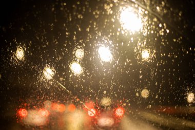 Yağmurda trafik sıkışıklığı sırasında parlak ışıkları olan ve geç kalan bir arabanın ön camındaki bulanık arka plan.