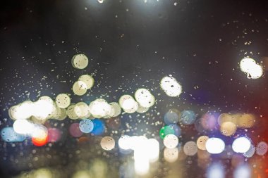 Yağmurda trafik sıkışıklığı sırasında parlak ışıkları olan bir arabanın ön camındaki bulanık arkaplan.