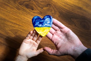 Çocukların ve erkeklerin avuçlarında Ukrayna bayrağı şeklinde kahverengi bir arka planda bir kalp, Ukrayna 'daki savaş.