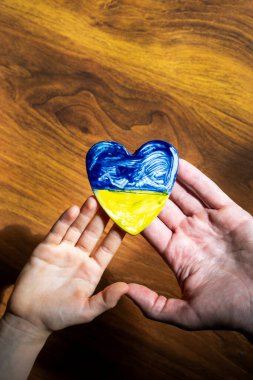 Çocukların ve erkeklerin avuçlarında Ukrayna bayrağı şeklinde kahverengi bir arka planda bir kalp, Ukrayna 'daki savaş.