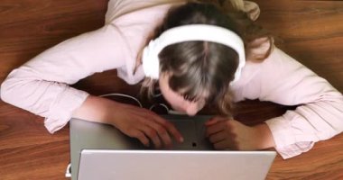 happy teen girl lies on the floor with a laptop and headphones and listens to music, learning