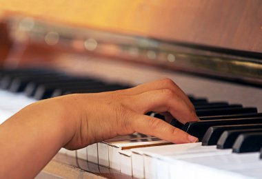 Genç bir piyanistin sağ elini tutuyor piyanonun beyaz tuşları üzerinde egzersiz yapıyor, müzik eğitimi alıyor.