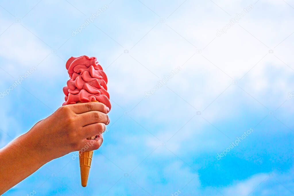 children's hand holds a huge pink ice cream with a cone against the blue sky, Use for advertising. horizonta