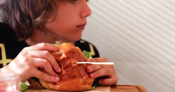 Ein Fröhlicher Junge Beißt Einem Café Einen Riesigen Hamburger Mit — Stockvideo