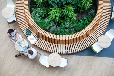 Genç bir kadın ve erkek, yeşil bitkilerle çevrili bir alışveriş merkezinde modern bir yerde yemek yiyorlar. Yukarıdan görünüm