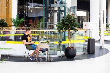 young man eats in a modern interior in the tcr and pokes his nose writes a message with green plants close-up. view from above