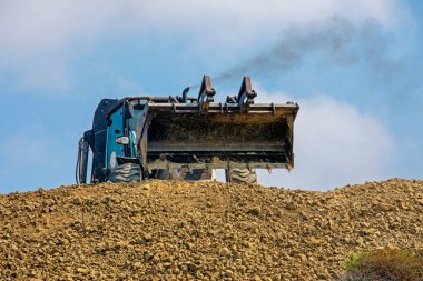 full bucket with the earth of an escalator frontally on a sunny hot day pours out against the sky.Global construction. Bottom vie