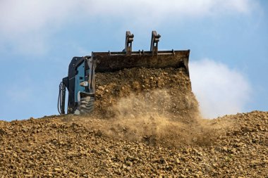 large bucket with an escalator pouring soil frontally on a sunny hot day against the sky. Global construction