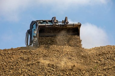 tractor with a large bucket with loose soil levels the road on a sunny hot day against the sky. Global construction. Mining, salt
