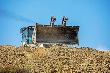 large empty escalator bucket frontally pours soil against the sky on a sunny hot day. Global construction. Bottom view