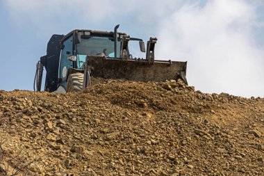 tractor with a big bucket aligns the road on a sunny hot day against the sky. Global construction. Mining, salt
