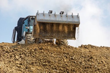 tractor with a large bucket of soil levels the road on a sunny hot day against the sky. Global construction.