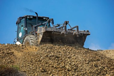 large bucket with the earth of an escalator frontally on a sunny hot day pours soil against the sky.Global construction. Bottom view