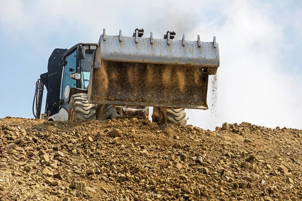 tractor with a large bucket of soil levels the road on a sunny hot day against the sky. Global construction.