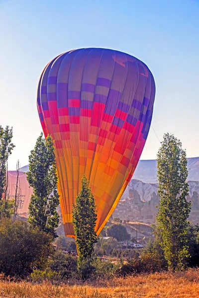 huge multi-colored balloon landed on the ground in Cappadocia against the sun after flying at dawn, on the goreme hills