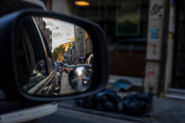 reflection of huge traffic in the right car mirror in the evening at sunset in a city of a million people with garbage on the sidewalk. Traffi