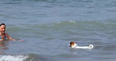  happy girl in swimming goggles swims teaches jack russell terrier to swim in the sea on a sunny day. Family holiday.