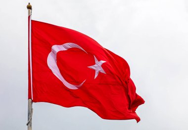 Turkish flag on the flagpole is fluttering against the background of a cloudy sky during the day.