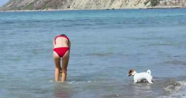  happy teenage girl in a red swimsuit plays with a jack russell terrier in a ball on the sea. Family holiday