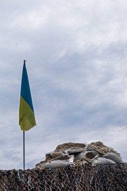 Bulutlu bir günde Ukrayna kamuflaj bayrağı askeri ağ ve kum torbalarıyla kontrol noktası. Ukrayna 'da savaş, dikey