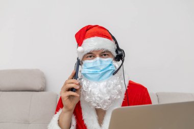 Noel Baba gibi giyinmiş, kulaklık takmış, dizüstü bilgisayarlı bir adam.